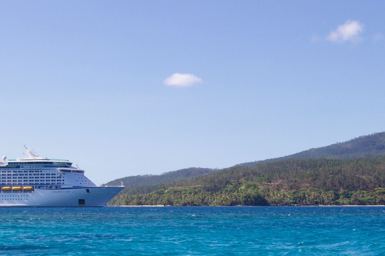 A large cruise ship anchored off a green tropical island in turquoise water
