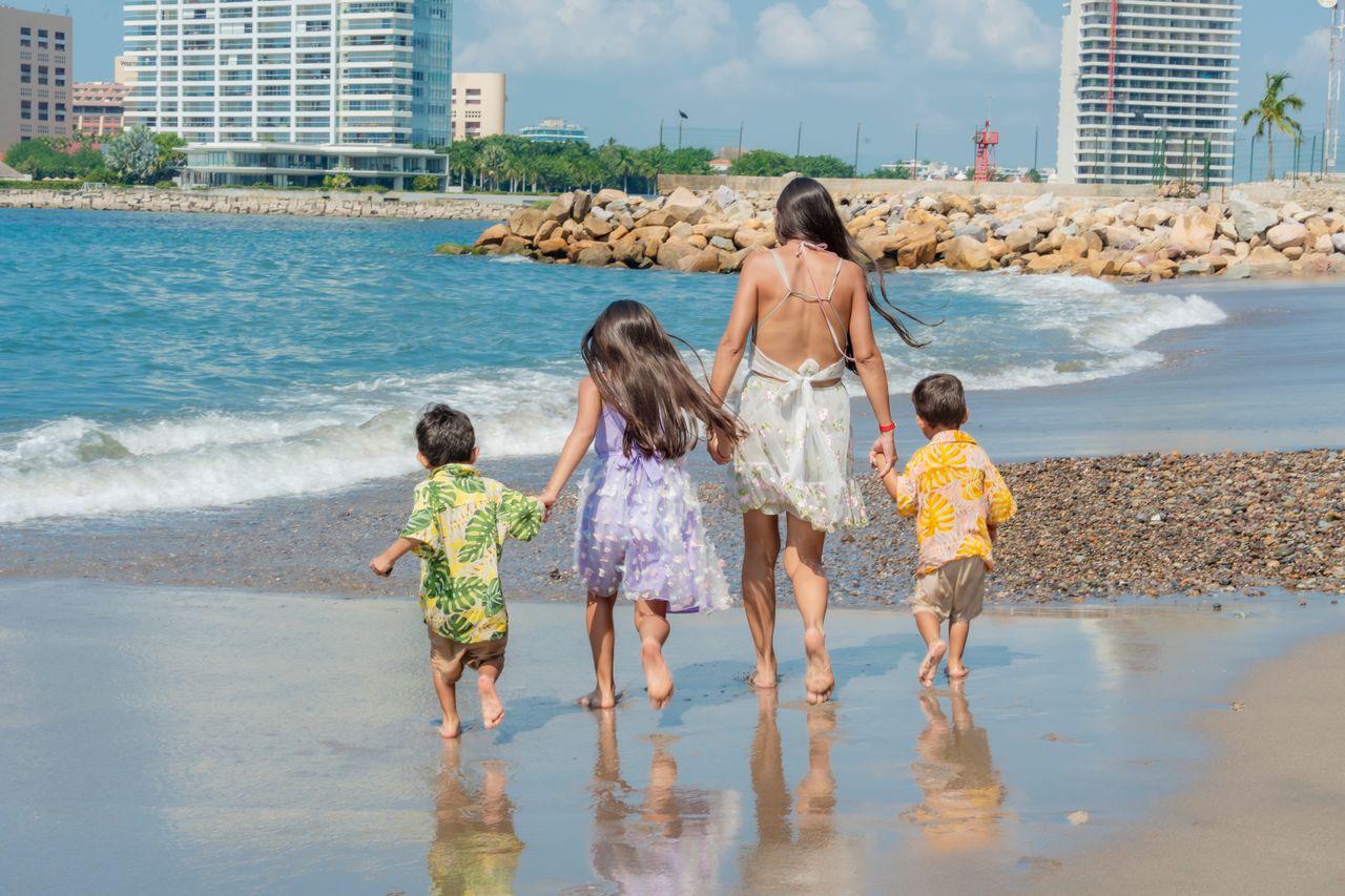 A parent walking along a sunny beach with two children near the water's edge