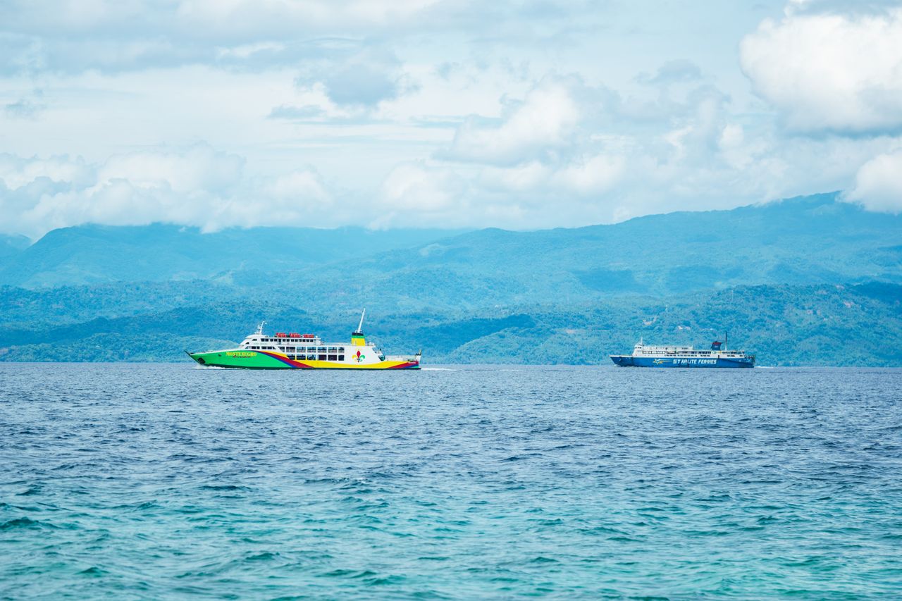 Passenger ferries crossing blue sea toward forested island mountains
