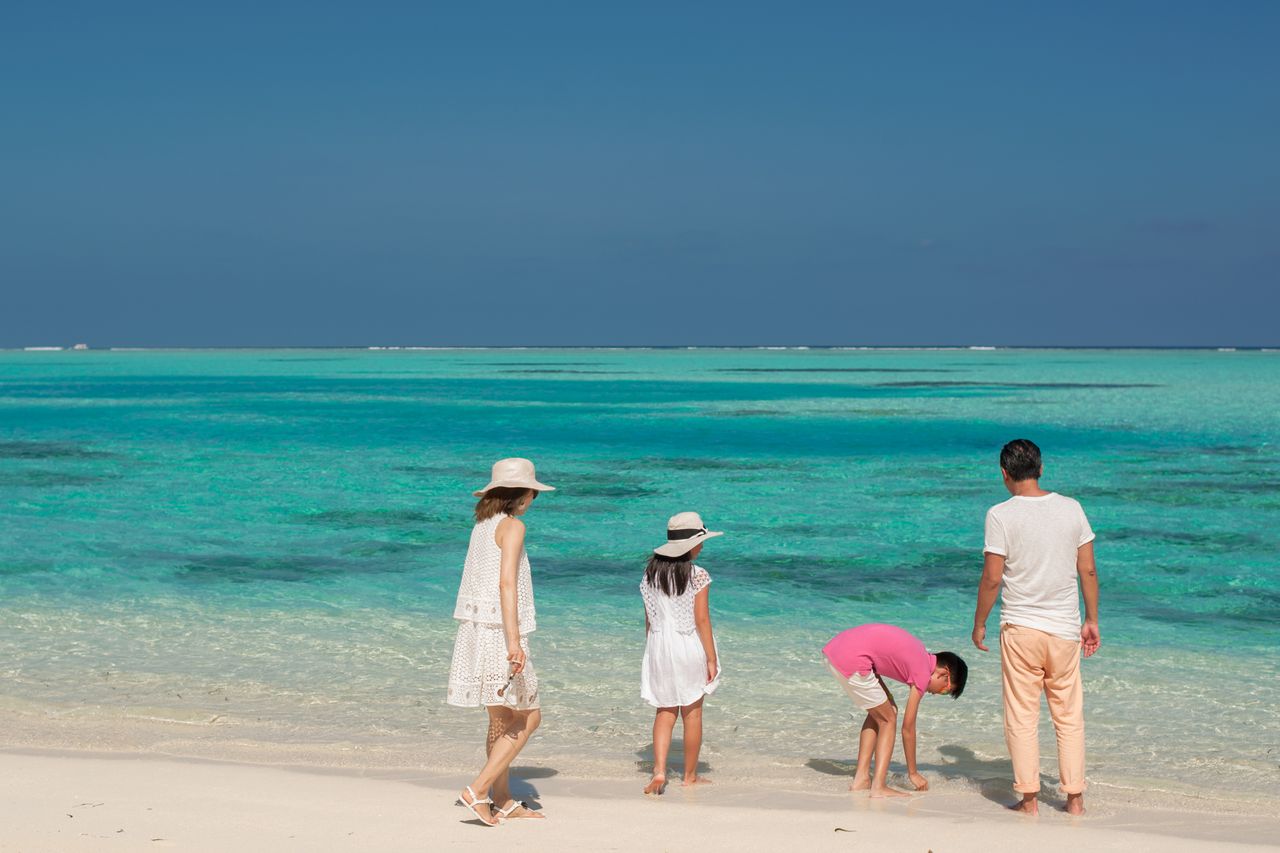 A family of four in shallow turquoise water at a tropical beach, evocative of Langkawi