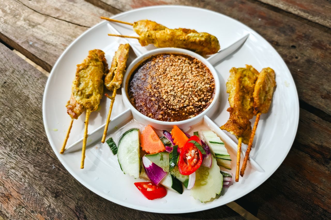 A plate of Malaysian satay skewers with peanut sauce and cucumber salad