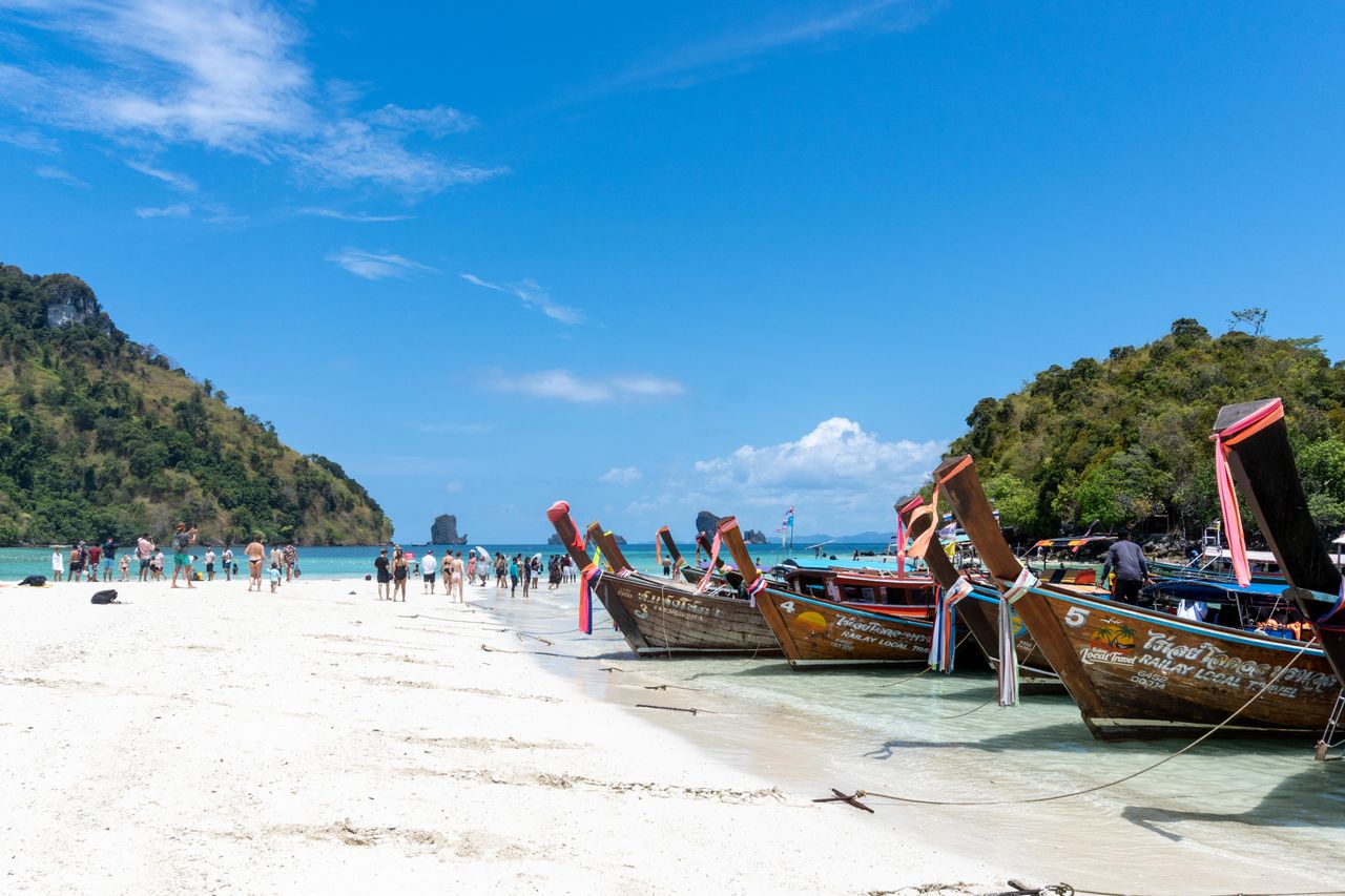 Traditional longtail boats on a busy Andaman Sea beach with limestone islands behind