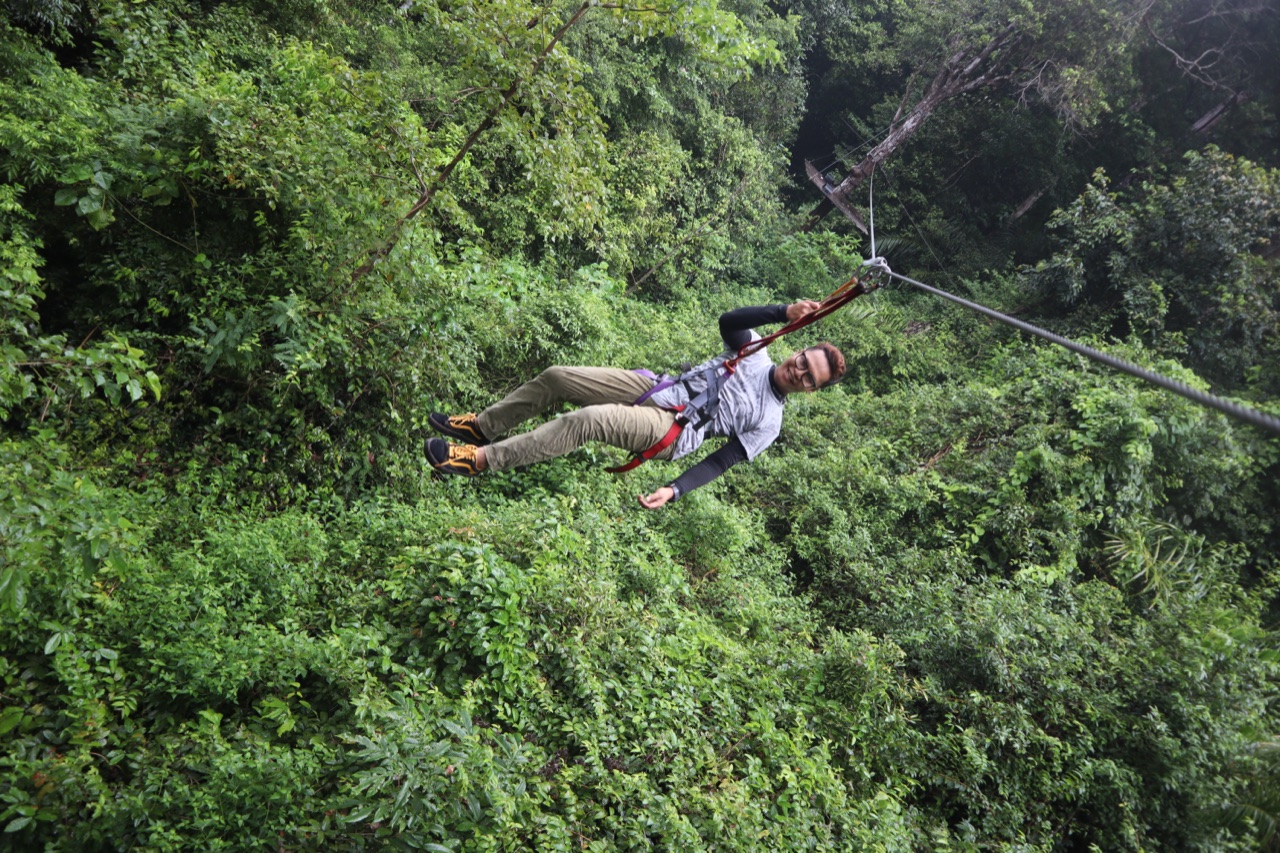 A harnessed visitor riding a flying fox zip line across the forest canopy at SKYTREX Langkawi